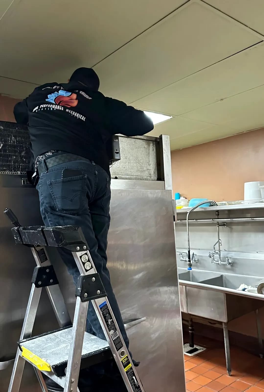 Technician on a ladder servicing equipment in a commercial kitchen